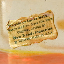 Sticker reads ‘Napkin or Letter Holder – Handmade from glass-like resin – Original design by New Trends Industries – Copyright MCMLXIX – Made in the U.S.A.’
