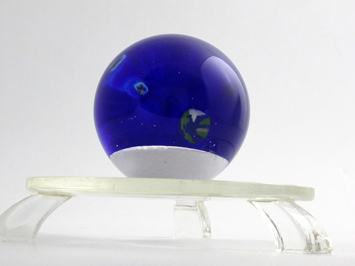 The paperweight depicts the view of the earth from the moon. As you turn the paperweight, the earth appears to rise on the horizon. Small sliced and stretched canes are added internally depicting galaxies.