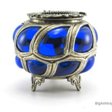 Antique Cobalt blue caged glass ashtray bowl. The artist blew the glass parison directly into the hand-formed metal cage coating the interior in a thick layer of rich cobalt blue glass and causing it to bulge out of the metal openings. This exceptional decor method is a revival of Roman era glass, copied from excavated examples discovered in the 17th Century.