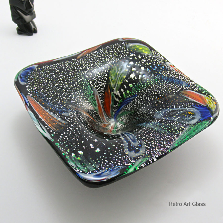 Unusual shaped square bowl with a deep round well in the center. Big, heavy and beautiful. Looks like a ‘black hole’ gobbling up galaxies. The murrine ‘galaxies’ are surrounded by large flake silver aventurine that look like distant stars.
